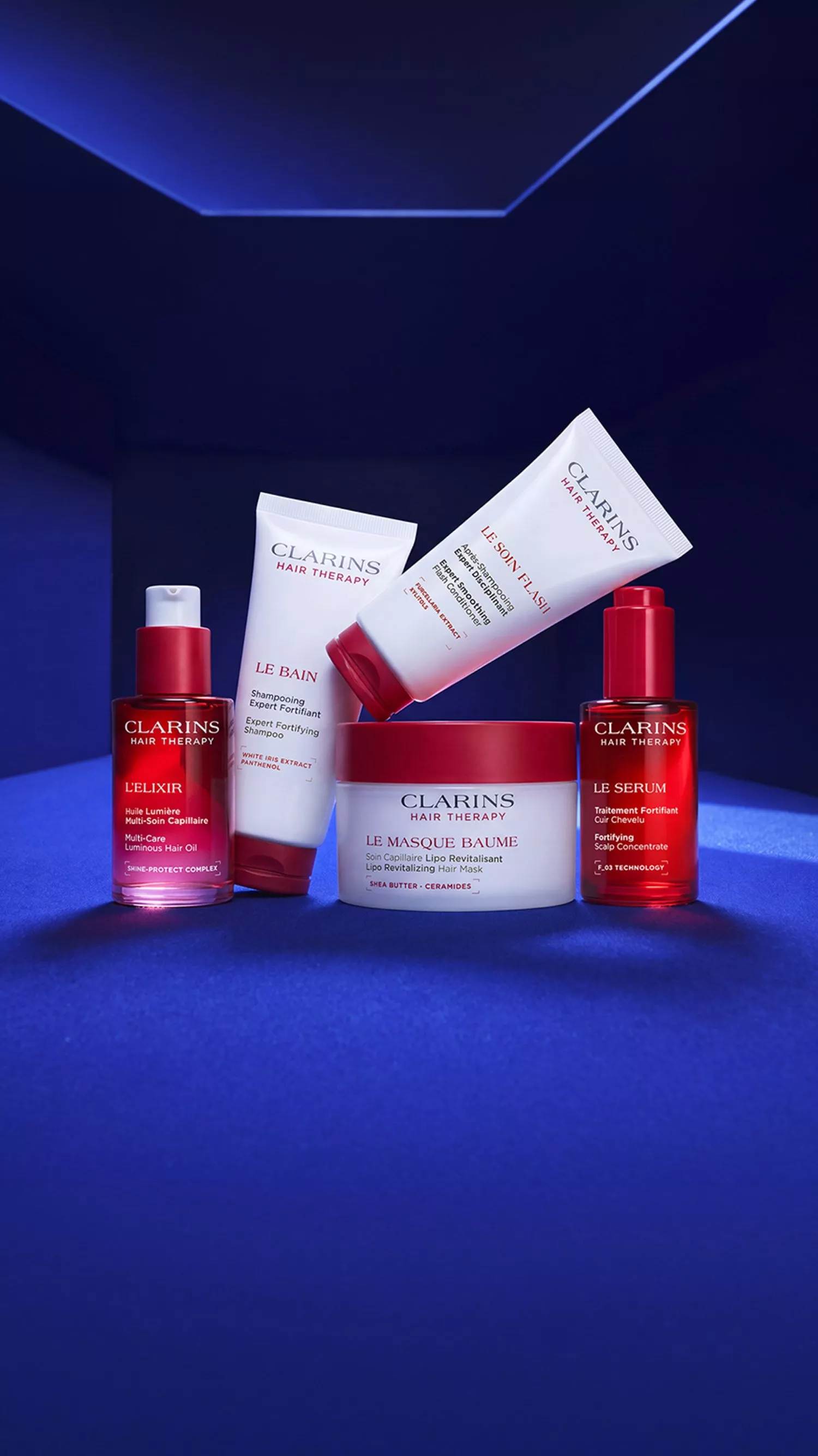 Clarins Hair Therapy range on blue backdrop: shampoo, scalp conditioner, oil elixir, mask and serum products