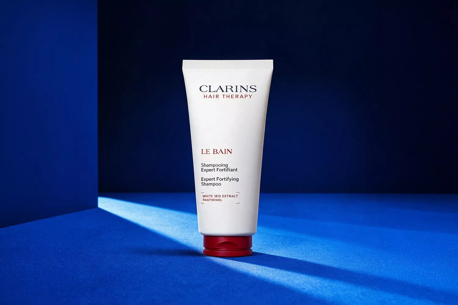 Clarins Hair Therapy Le Bain expert fortifying shampoo tube on blue background, studio product photograph