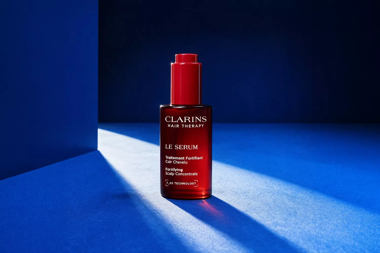 Clarins Hair Therapy Le Serum fortifying scalp concentrate bottle on blue background with dramatic studio lighting