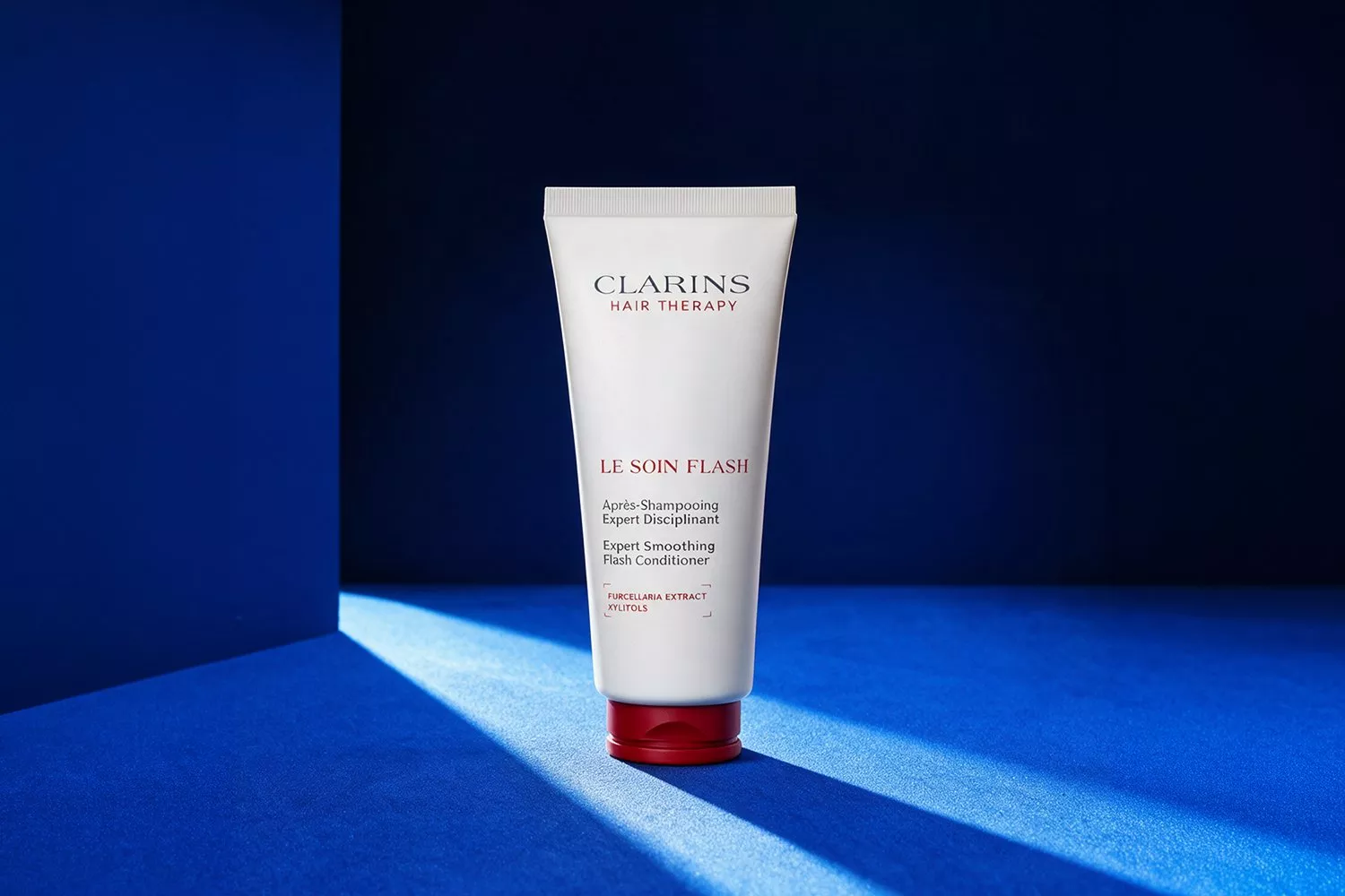 Clarins Hair Therapy Le Soin Flash smoothing conditioner tube on blue backdrop with dramatic light and shadow