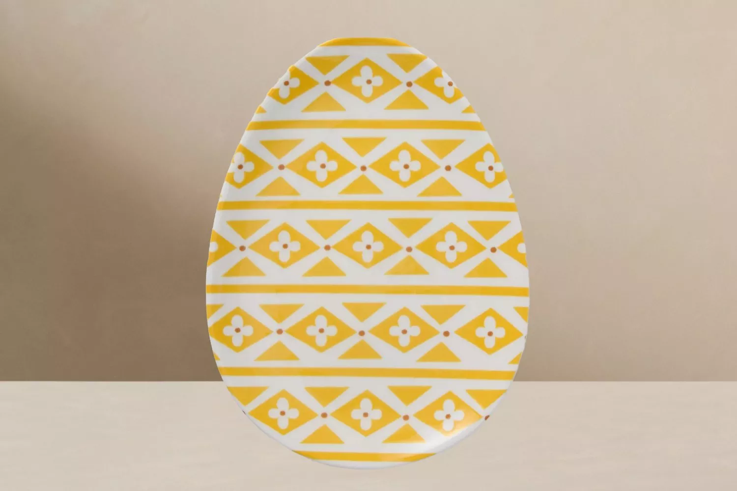 Oval plate with a yellow geometric pattern featuring triangles and flowers on a light background.
