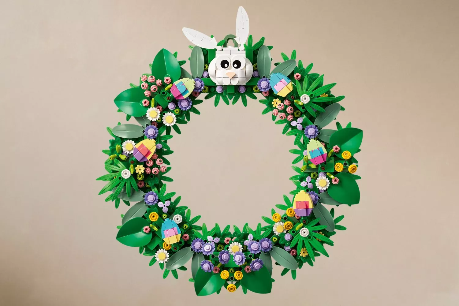 A colourful LEGO wreath with green leaves, pastel flowers, and a cute white bunny on top, set against a beige background.