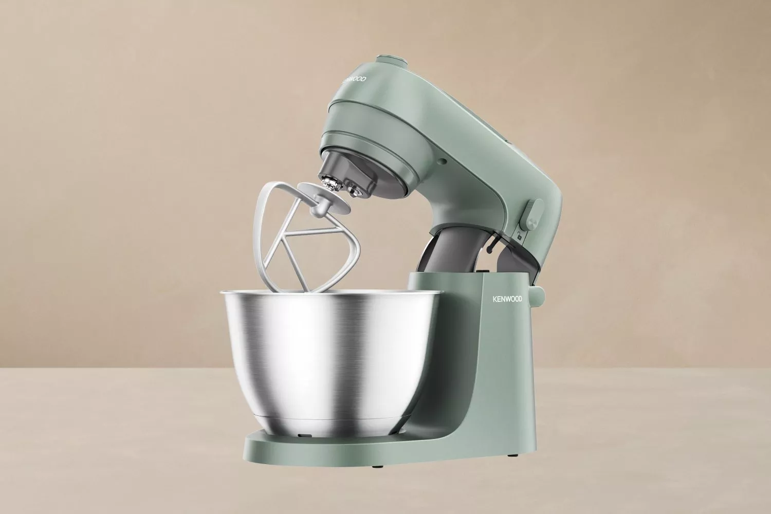 Stylish Kenwood stand mixer in green with a silver bowl and beater attachment, set against a beige background.