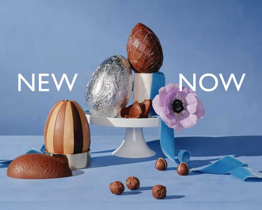  A display of easter eggs and chocolates on white china with blue ribbon and purple flower