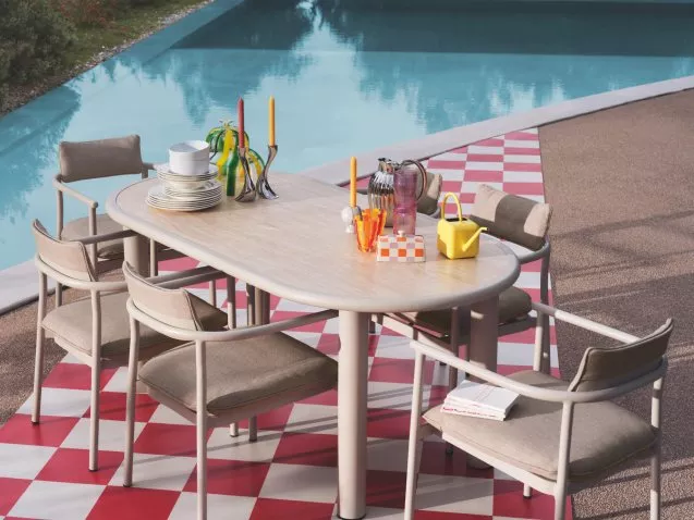 Modern outdoor dining table and chairs by a pool, styled with colourful glassware and tableware on patio.