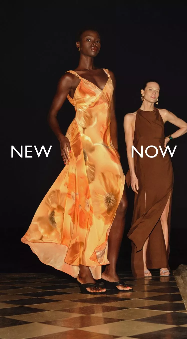 Two fashion models in flowing orange and brown dresses on a dark runway, new season womenswear campaign shot