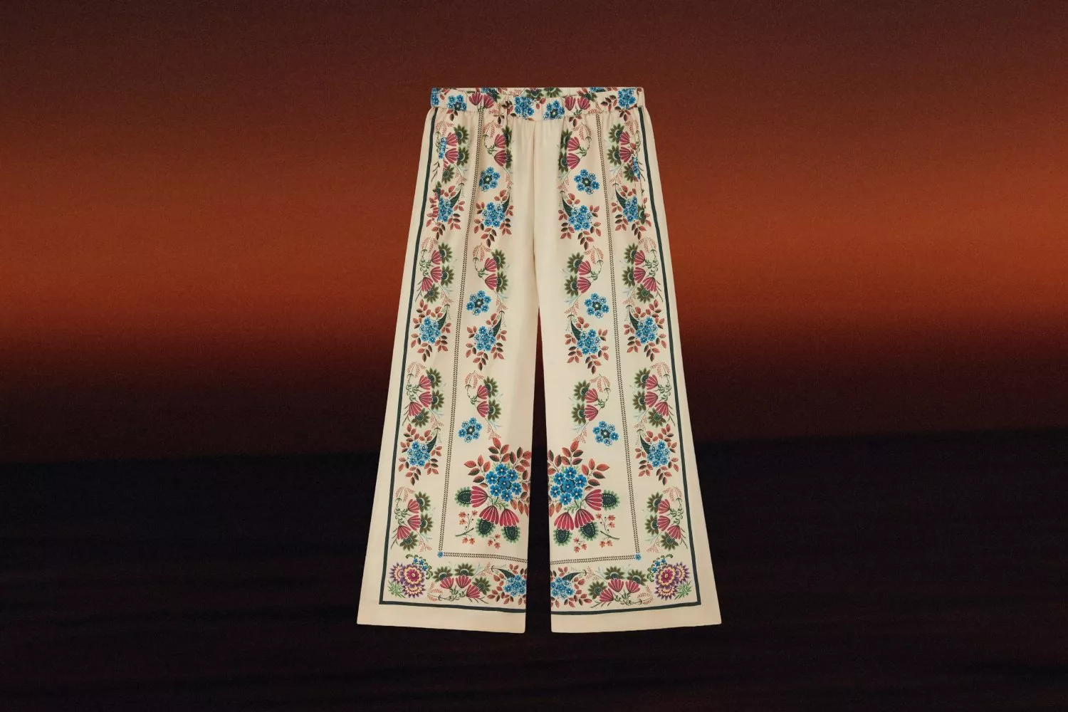 Cream wide-leg trousers with colourful floral print border, fashion flat lay on dark gradient background