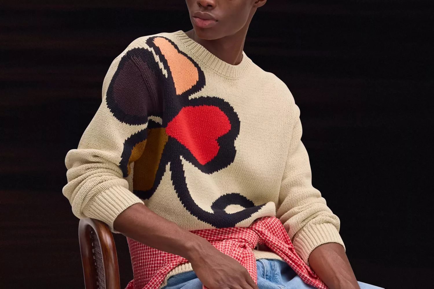 Model wearing cream knit jumper with bold floral pattern, layered with red gingham shirt and blue jeans