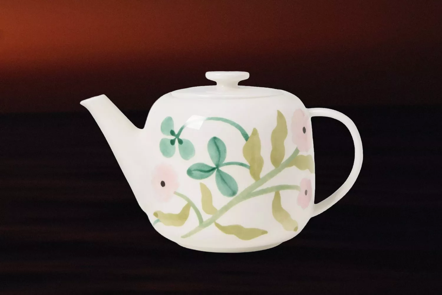 White ceramic teapot with lid and handle, decorated with pastel floral pattern, isolated on dark background