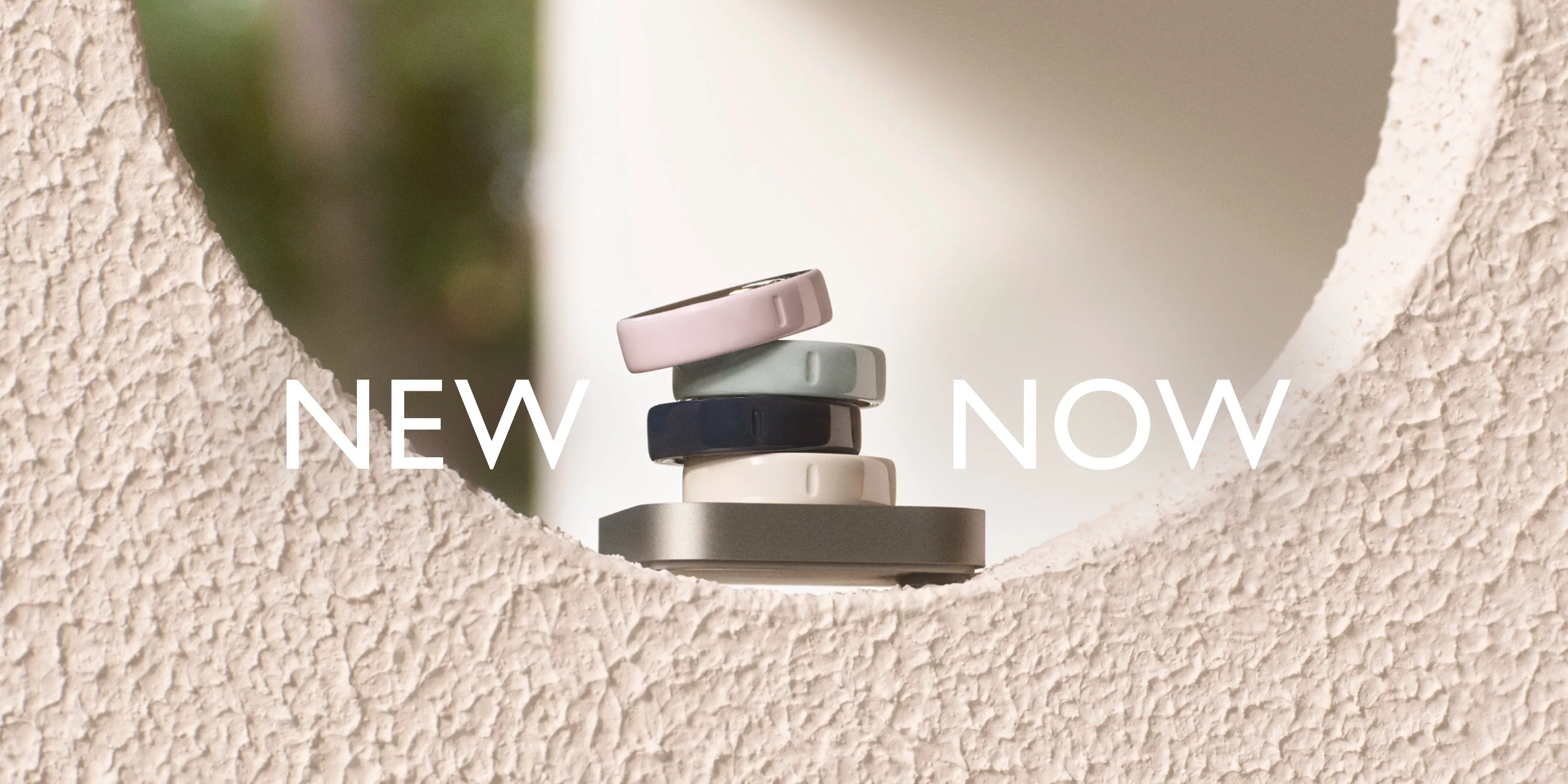 Stacked smart devices in various colours on textured surface, with "NEW NOW" text above.