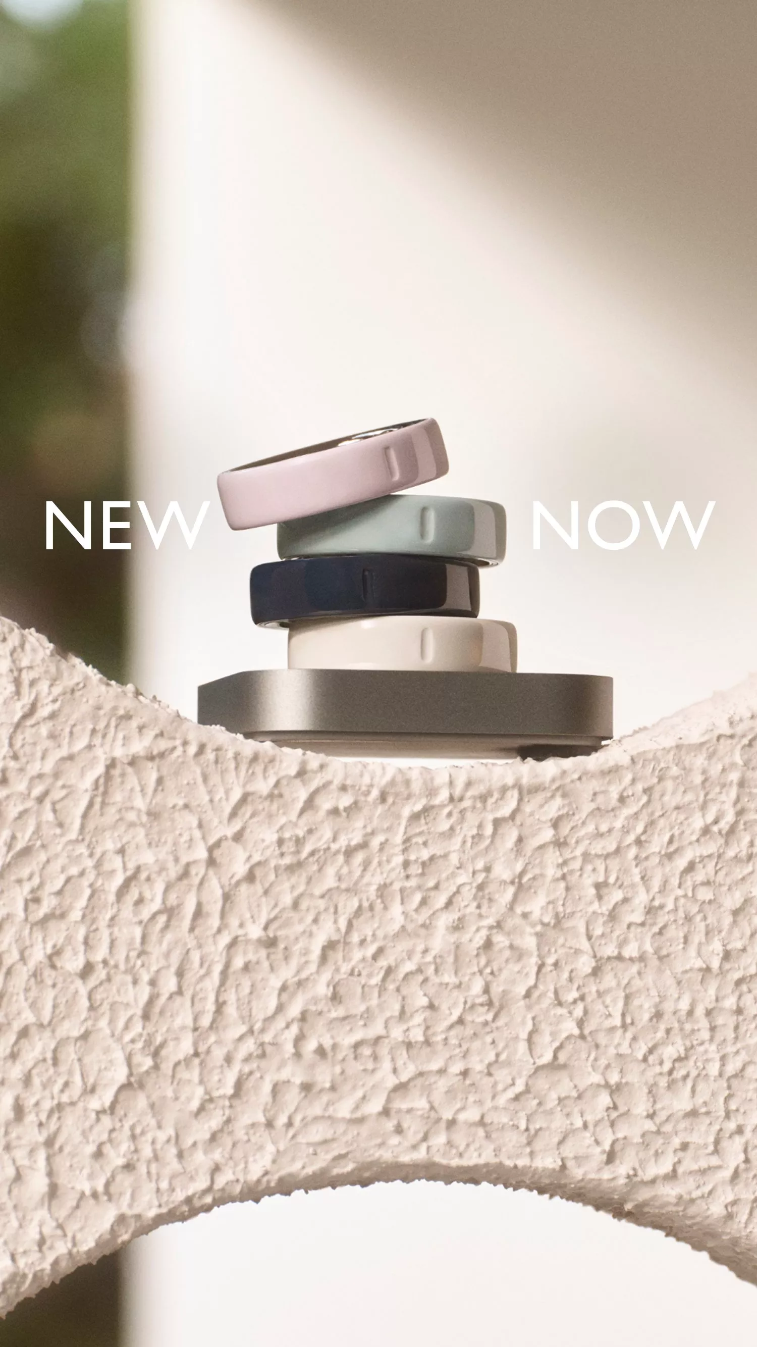 Stacked smart devices in various colours on textured surface, with "NEW NOW" text above.