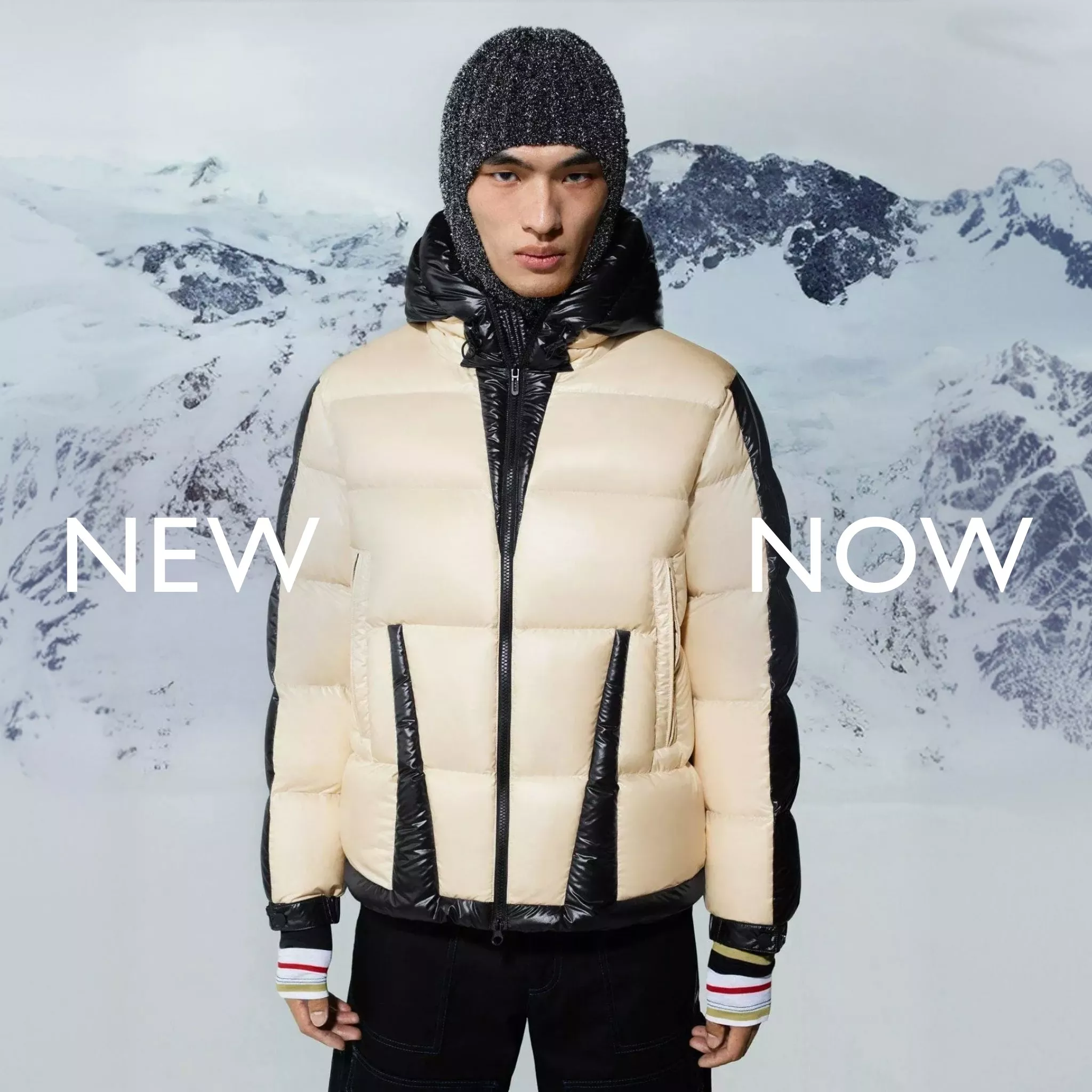 A man stands centered in a cream-colored puffer coat with black accents, wearing a dark knit hat.