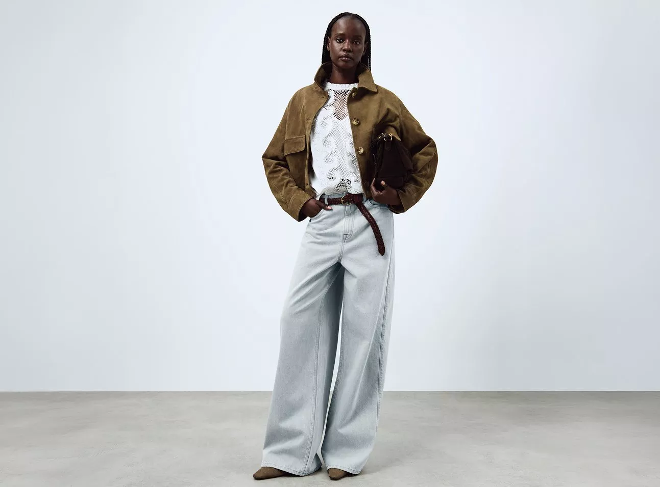 Woman in a brown jacket and white top, wearing light blue wide-leg jeans and holding a brown bag.
