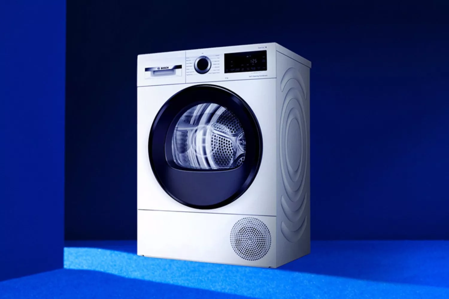 Front-loading tumble dryer with digital controls, white finish, shown on a blue studio background for home laundry appliances