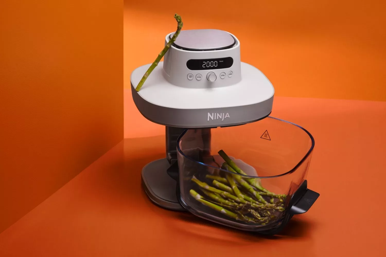 Ninja food processor with digital display and bowl of fresh asparagus on an orange studio background