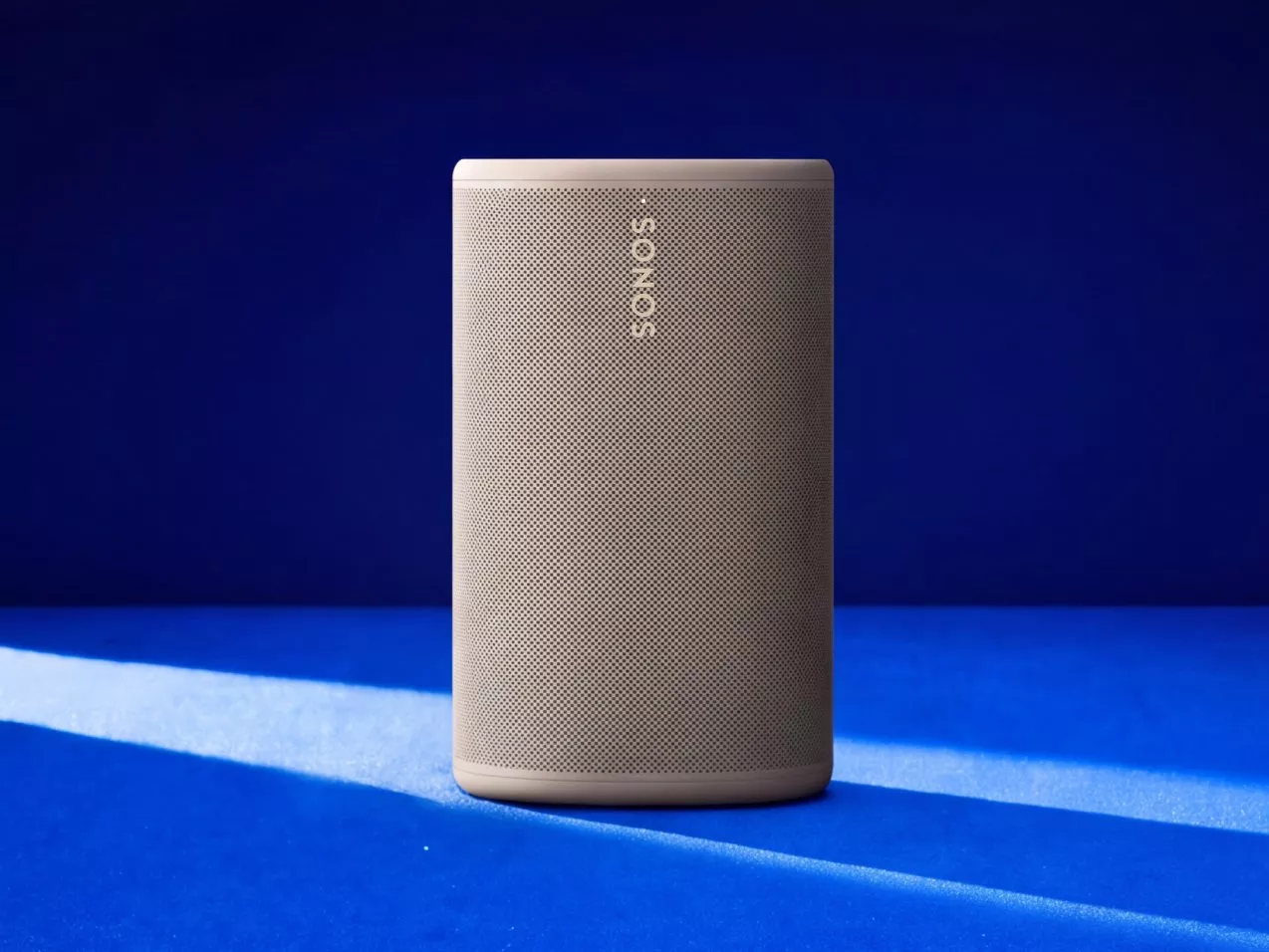 Beige Sonos wireless speaker on blue background, modern home audio system product photo with soft shadows