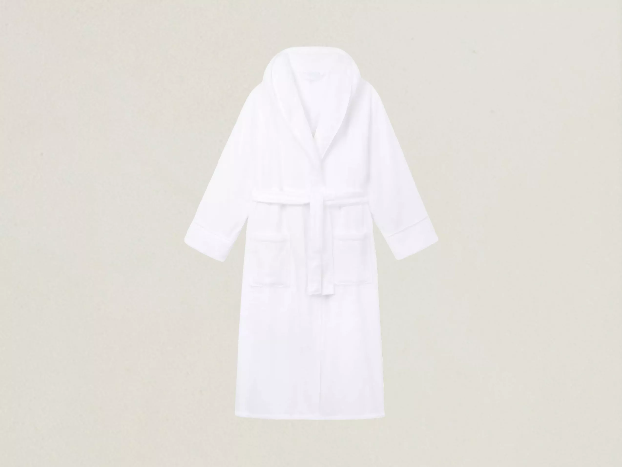 White cotton hotel-style bathrobe with shawl collar, belt tie and front pockets on a plain grey backdrop