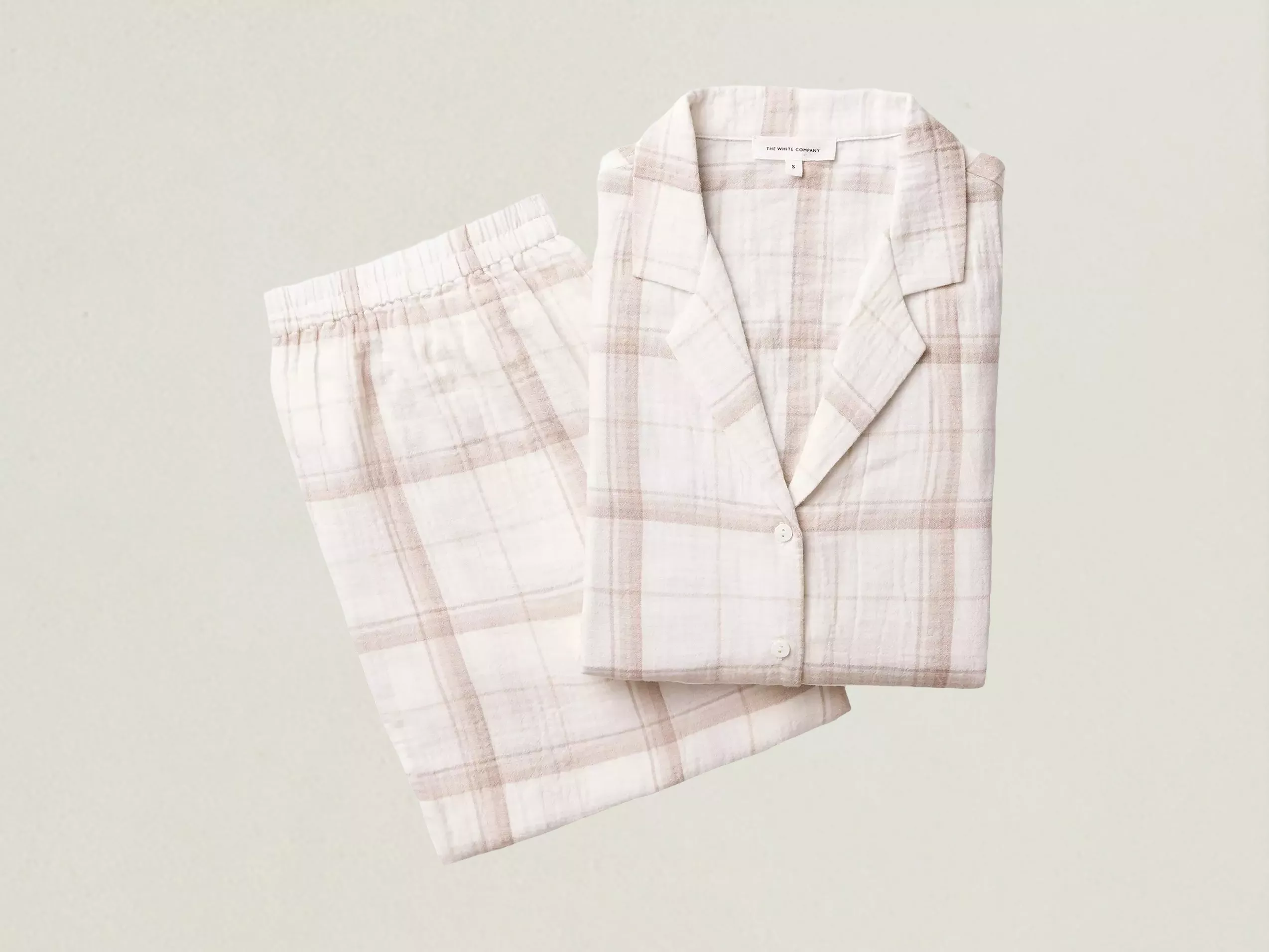 Soft cream and blush plaid cotton pyjama set with button-up top and elastic waist trousers, folded flat lay