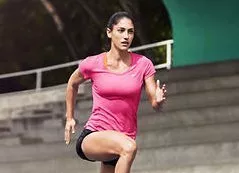 Athletic woman sprinting up stadium steps in pink sports top, outdoor fitness training workout session
