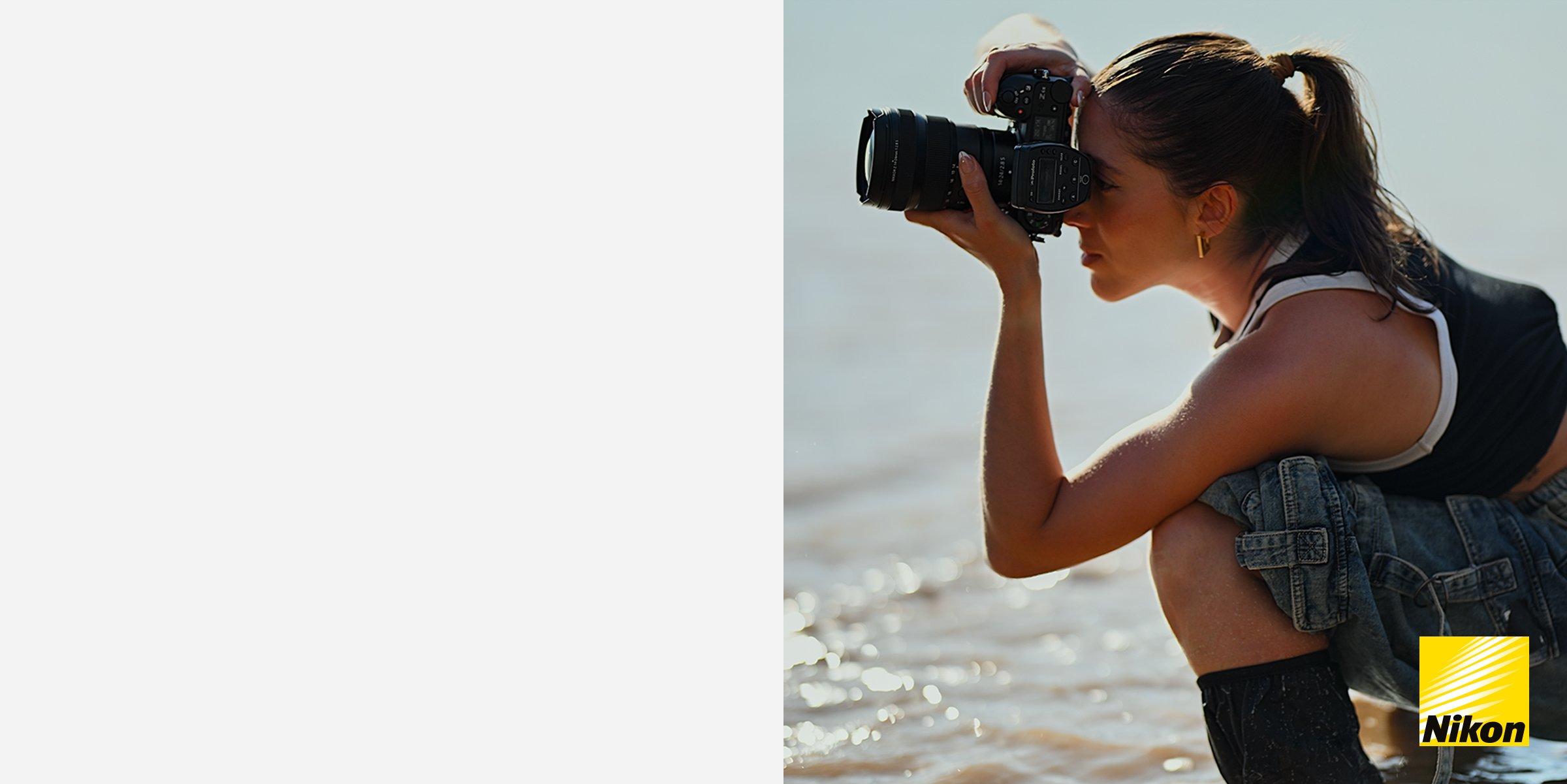 a women crouched down using a nikon slr camera on a beach