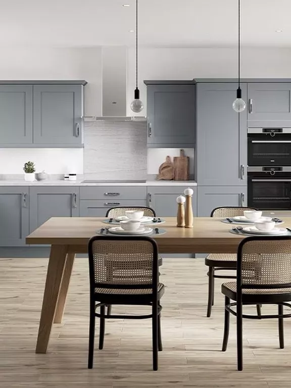 Modern kitchen with grey cabinets, a wooden dining table, black chairs, and minimalist lighting fixtures.
