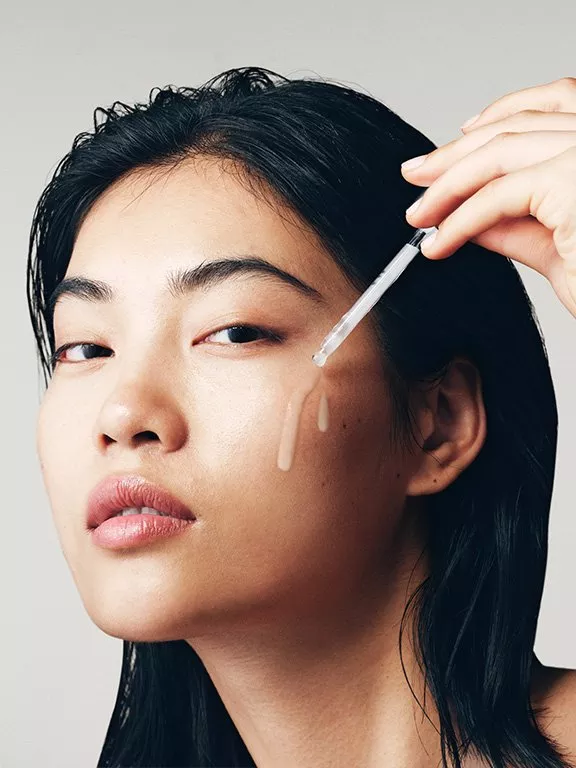 A person applying skincare serum on their cheek with a dropper, showcasing radiant and healthy skin.