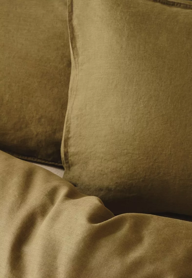 Luxurious olive green linen pillows and sheets, showcasing texture and inviting comfort in a cosy setting.