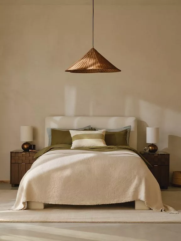 Minimalist bedroom with a neutral palette, featuring a wooden pendant light above a bed with decorative cushions.