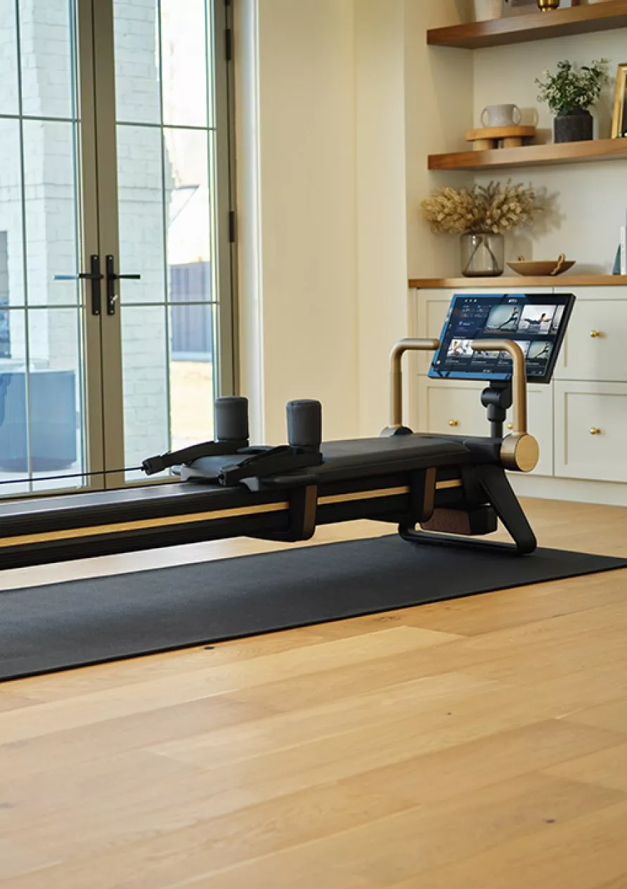 Smart home Pilates reformer machine with touchscreen, in bright living room by large window and plant
