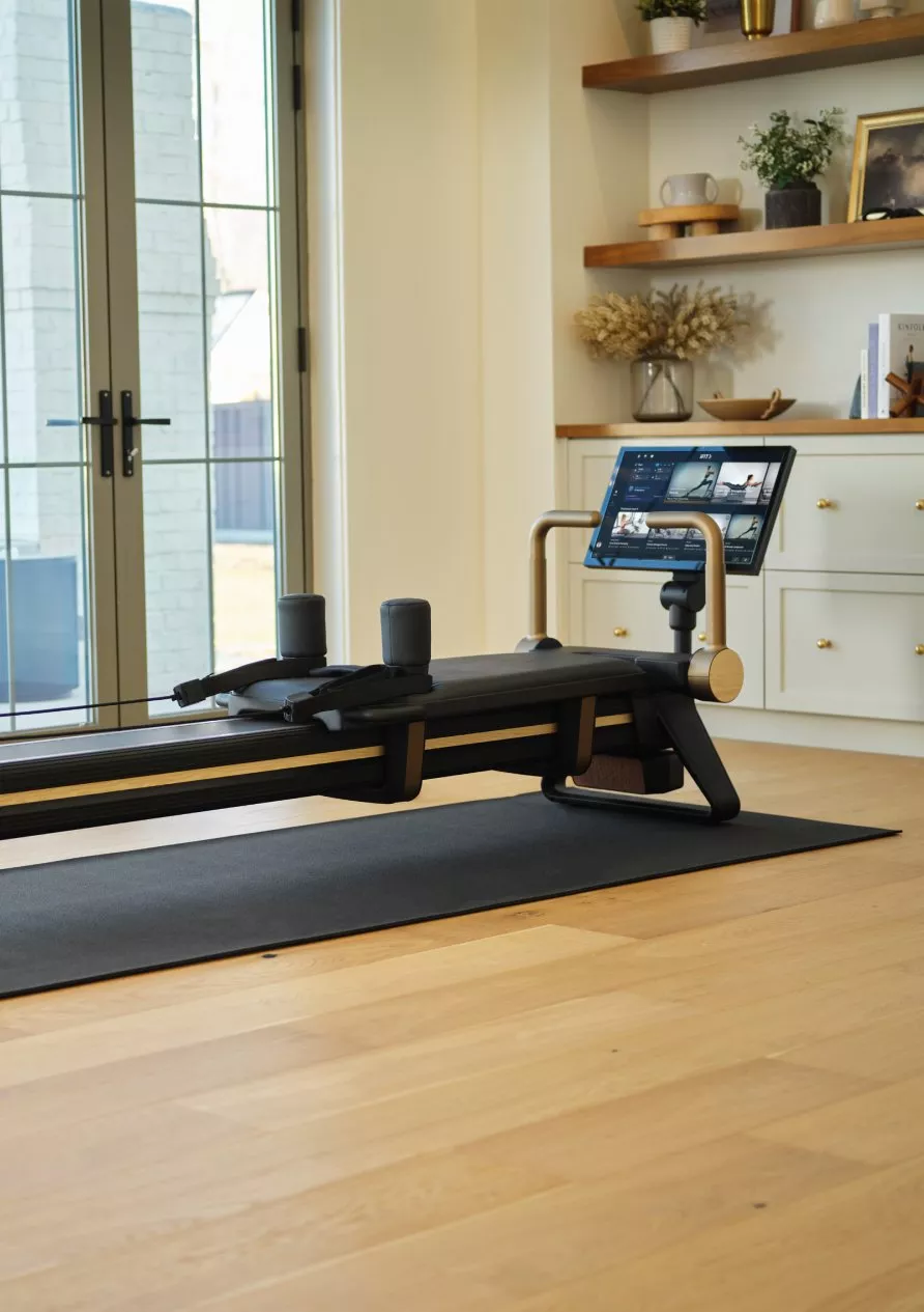 Smart home Pilates reformer machine with touchscreen, in bright living room by large window and plant