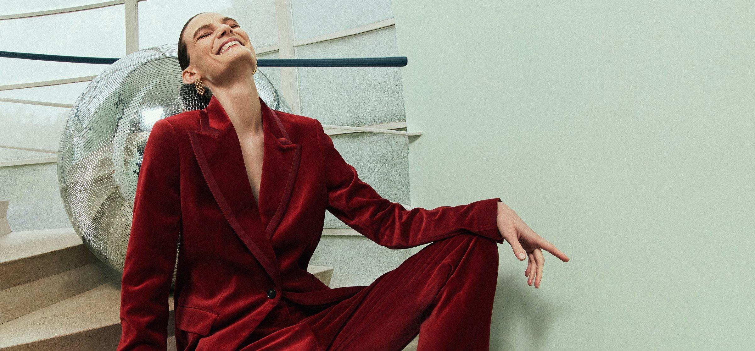 Image of a lady sitting on some stairs wearing a red velvet suit leaning on a mirrorball