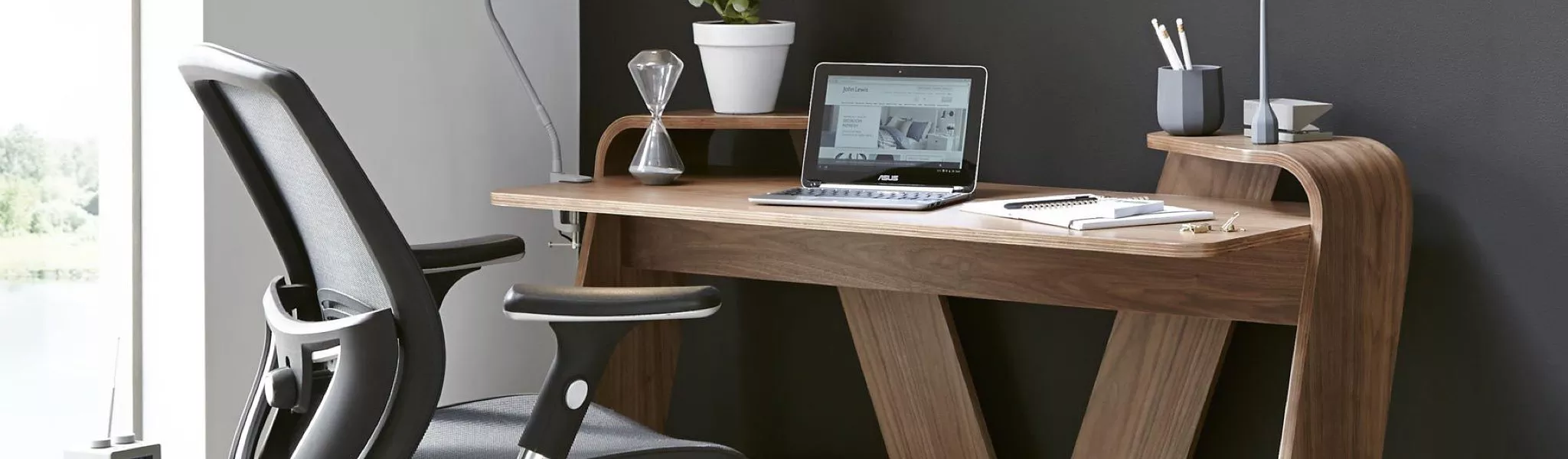 Modern home office setup with ergonomic chair, wooden desk, laptop, notepad, and desk lamp.