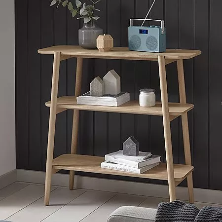 Stylish wooden shelving unit with books, a radio, decor pieces, and a vase, set against a dark panelled wall.