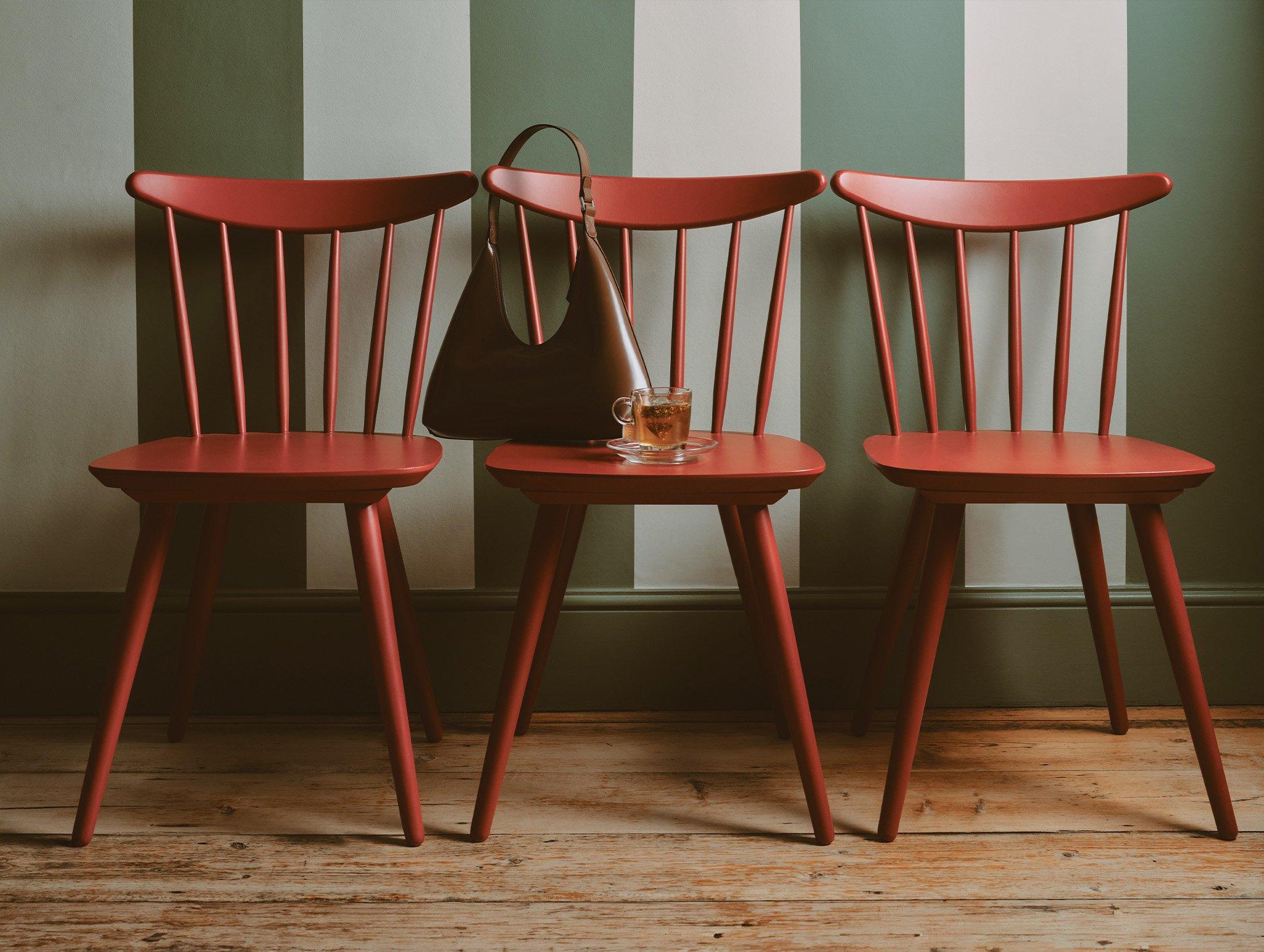 Three wooden chairs with handbag and cup of tea sitting on chair seat