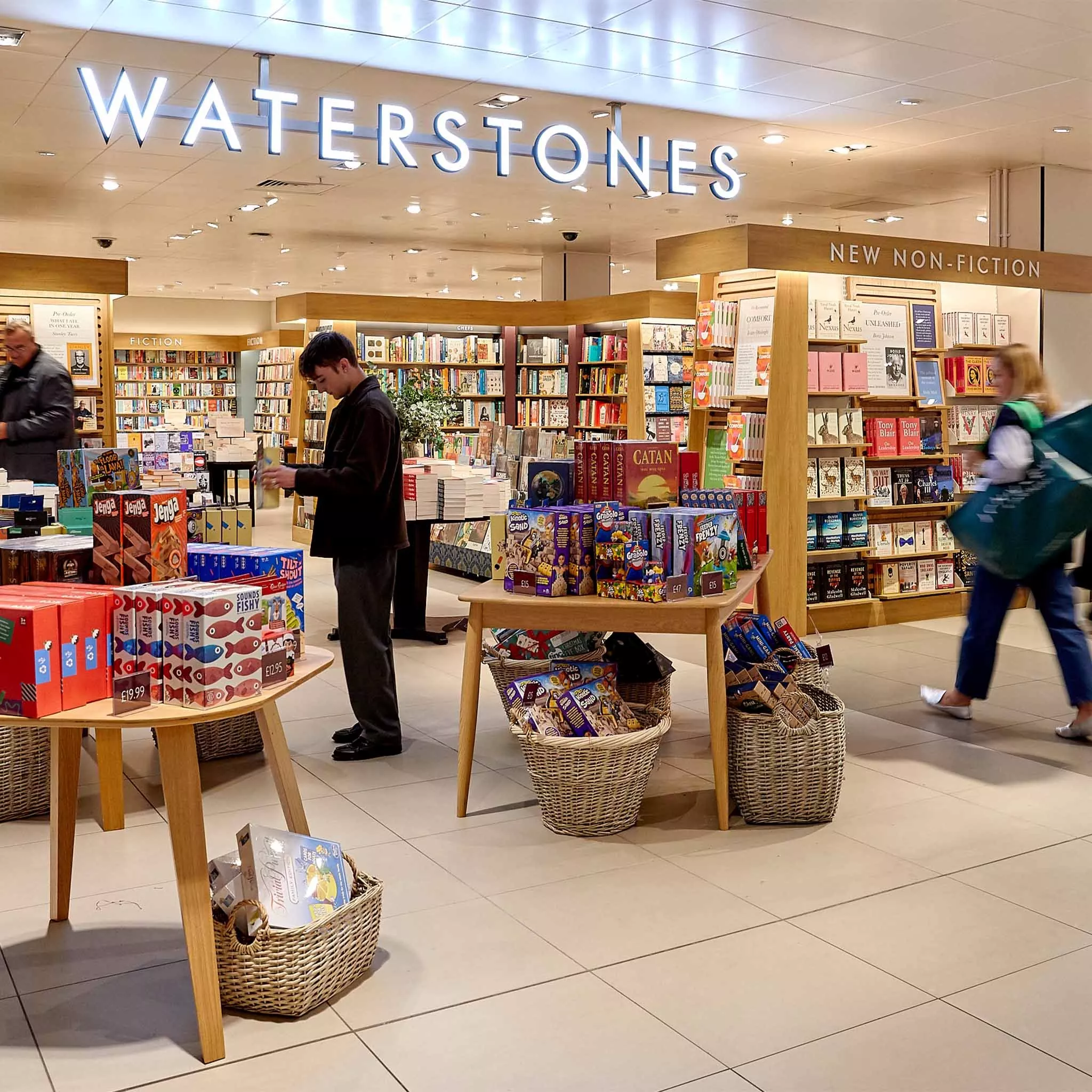 A bright Waterstones store showcasing books and board games, with tables and baskets filled with products.
