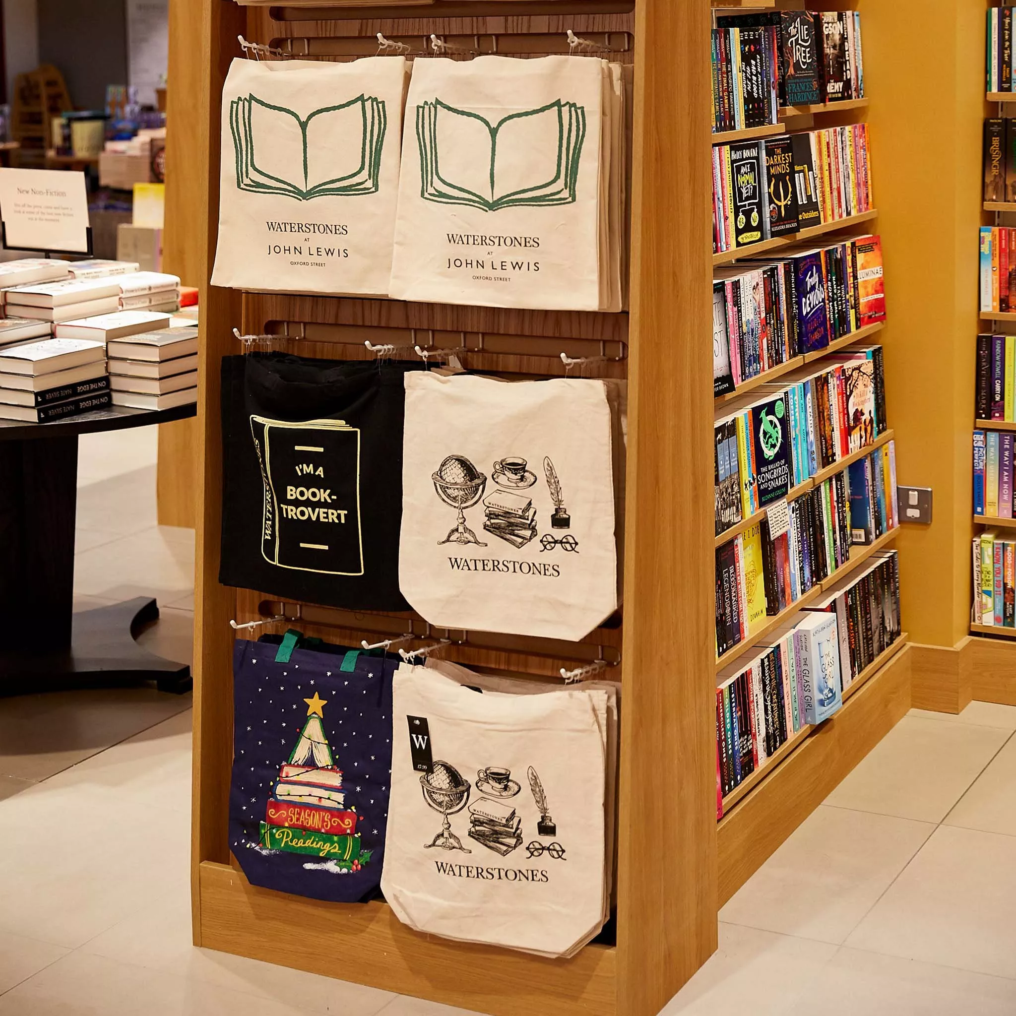Bookstore interior with tote bags on display, featuring literary designs. Bookshelves with colourful spines nearby.