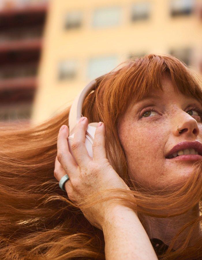 Close up of lady wearing headphones and the Oura Ring 4 Ceramic