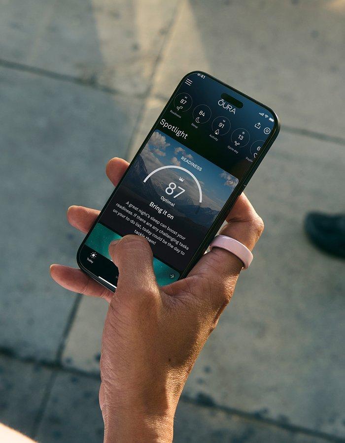 Close up of person holding a phone using the Oura app and wearing a Oura Ring 4 Ceramic