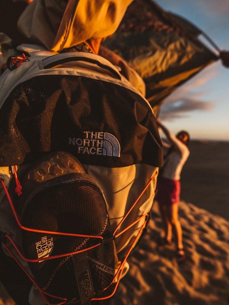 The North Face Woman tying her shoe laces on the top of a hill with sky in the background