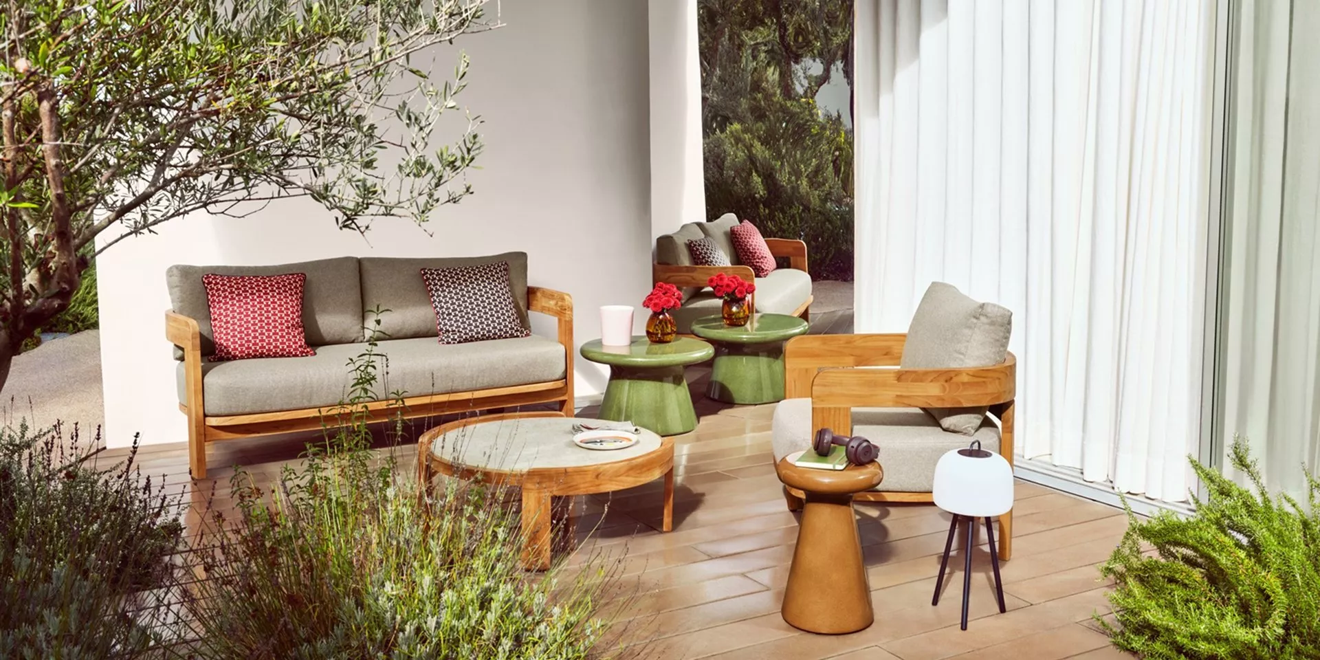 Modern outdoor patio lounge with teak sofa and armchair, grey cushions, side tables and garden greenery