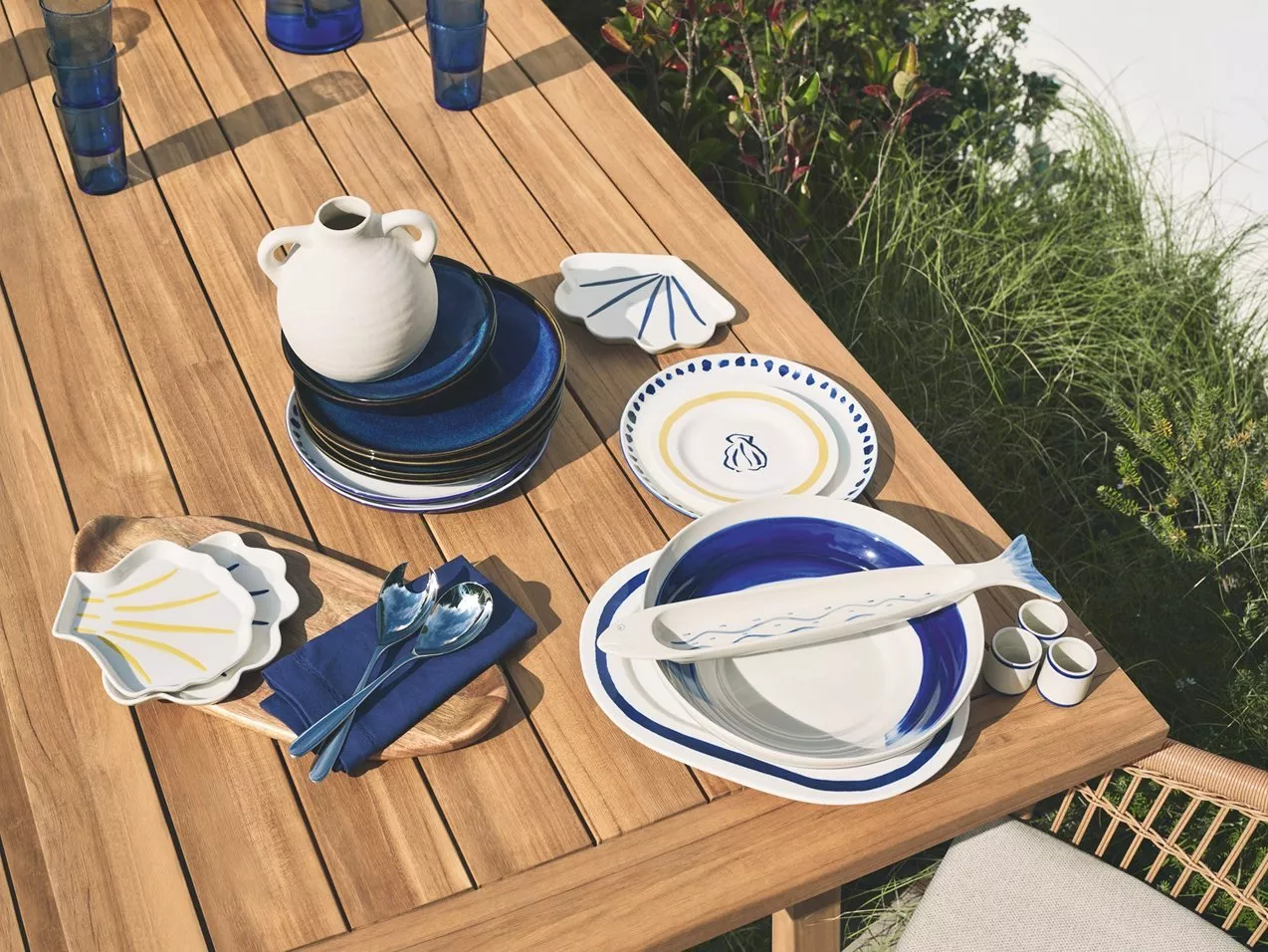 Outdoor dining table set with blue and white ceramic plates, fish platter, shell dishes and glasses in garden