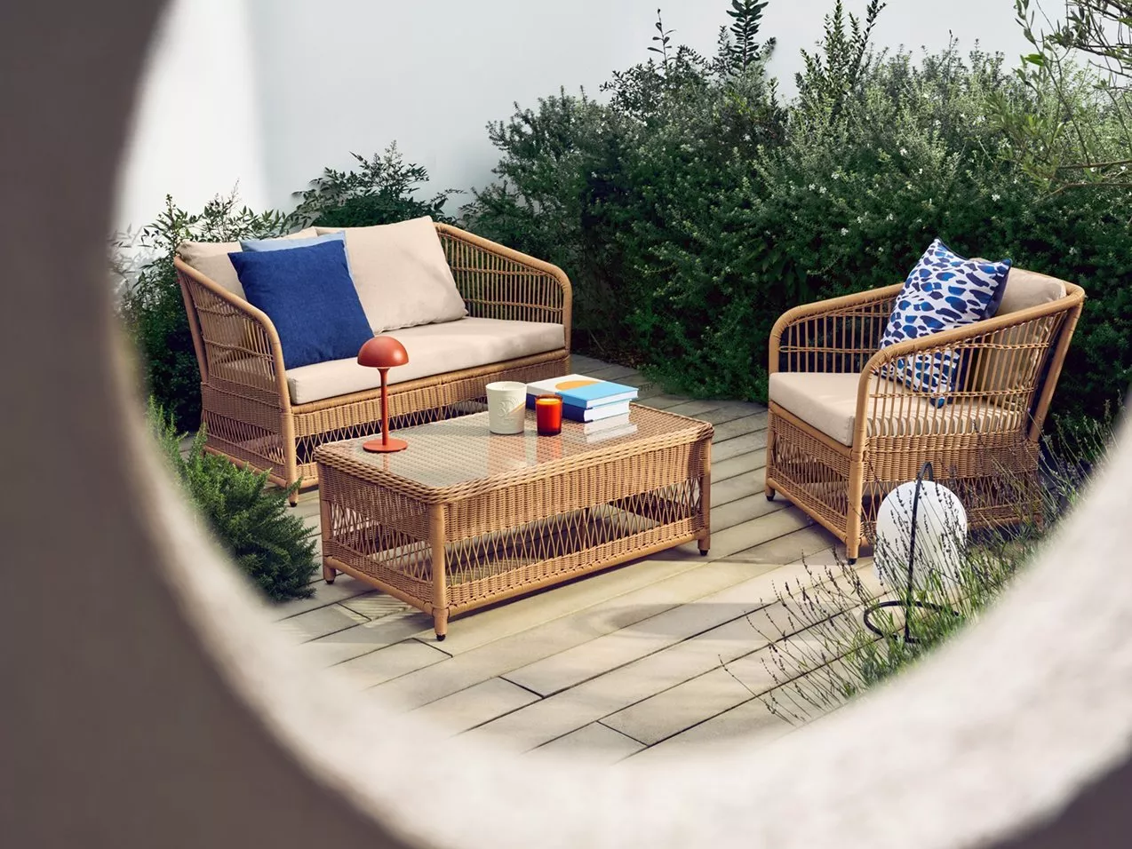 Rattan outdoor lounge set on patio with sofa, armchair and coffee table, blue cushions and décor items