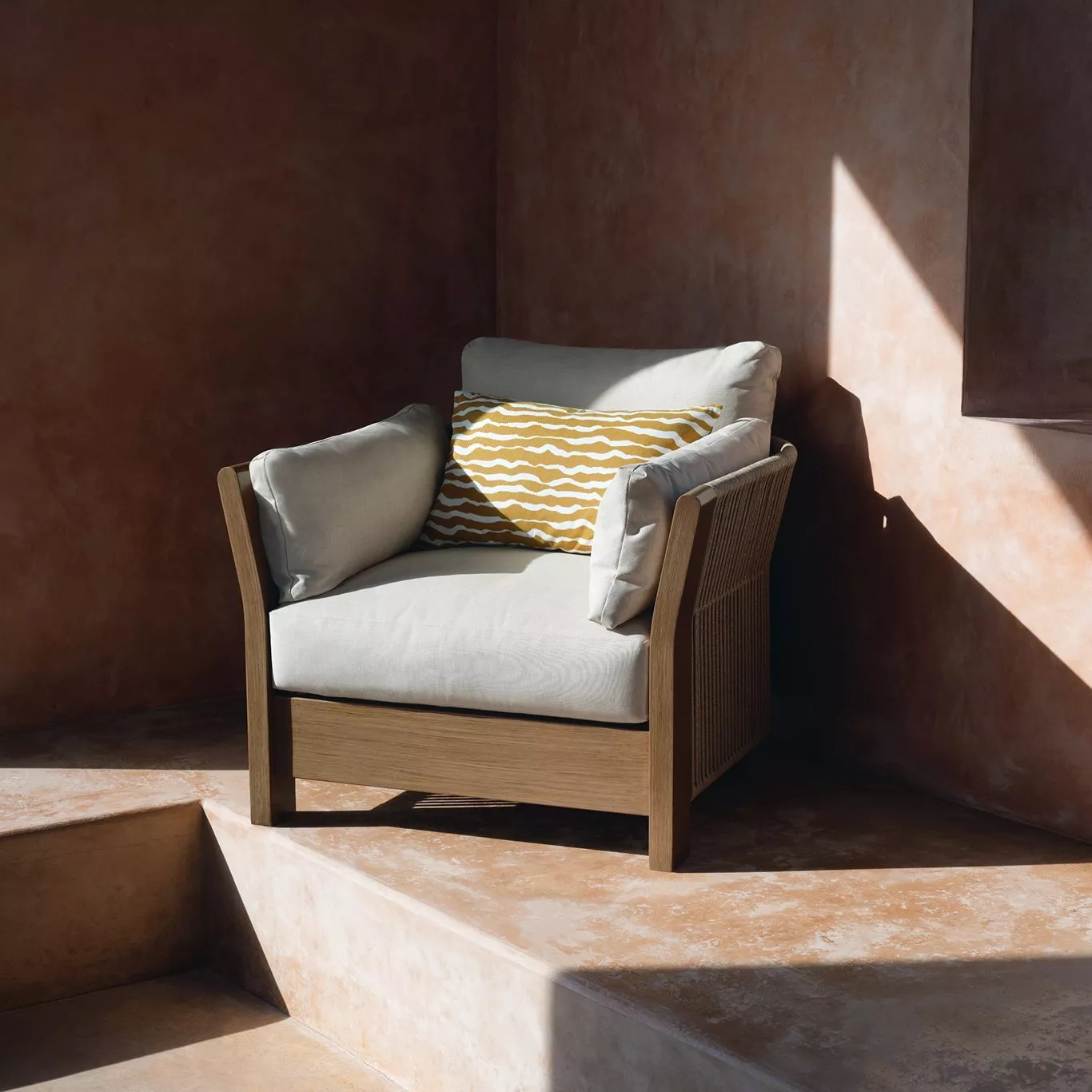 Modern outdoor lounge chair with wooden frame, cream cushions and yellow patterned pillow in sunlit patio corner