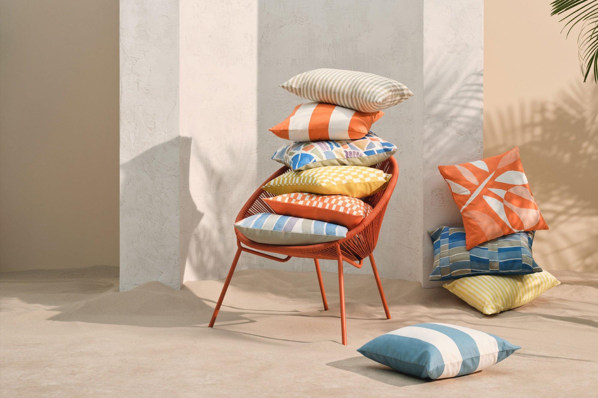 lots of cushions stacked on a outdoor chair, some on the floor, plain beige background