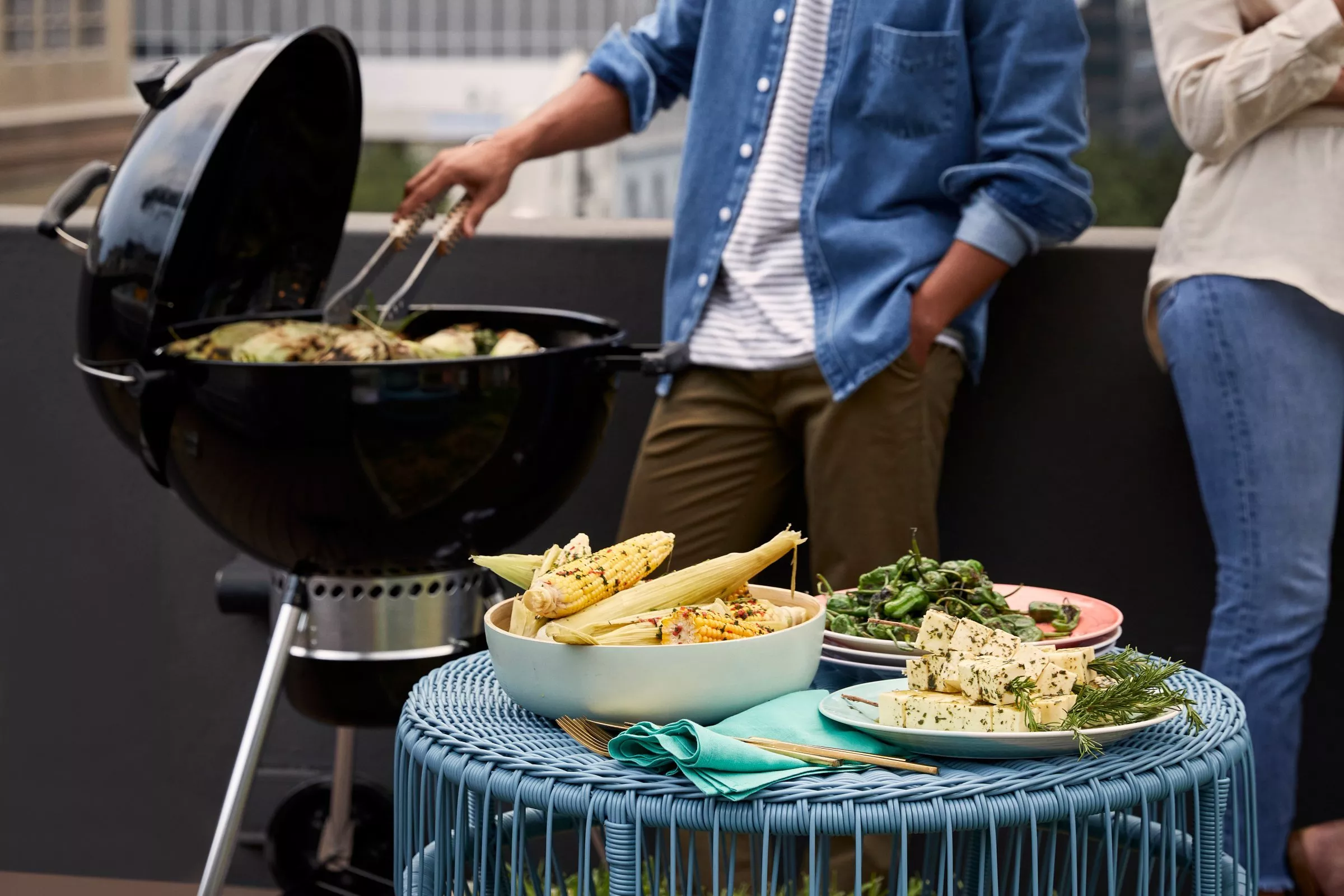 Outdoor barbecue on a balcony, grilling vegetables with corn on the cob and herbed tofu on a table