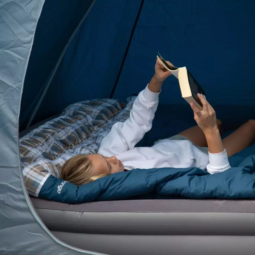 woman lying on a camping bed in a tent reading a book