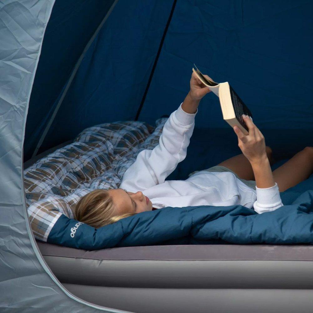 girl reading a book on a camping bed inside a tent