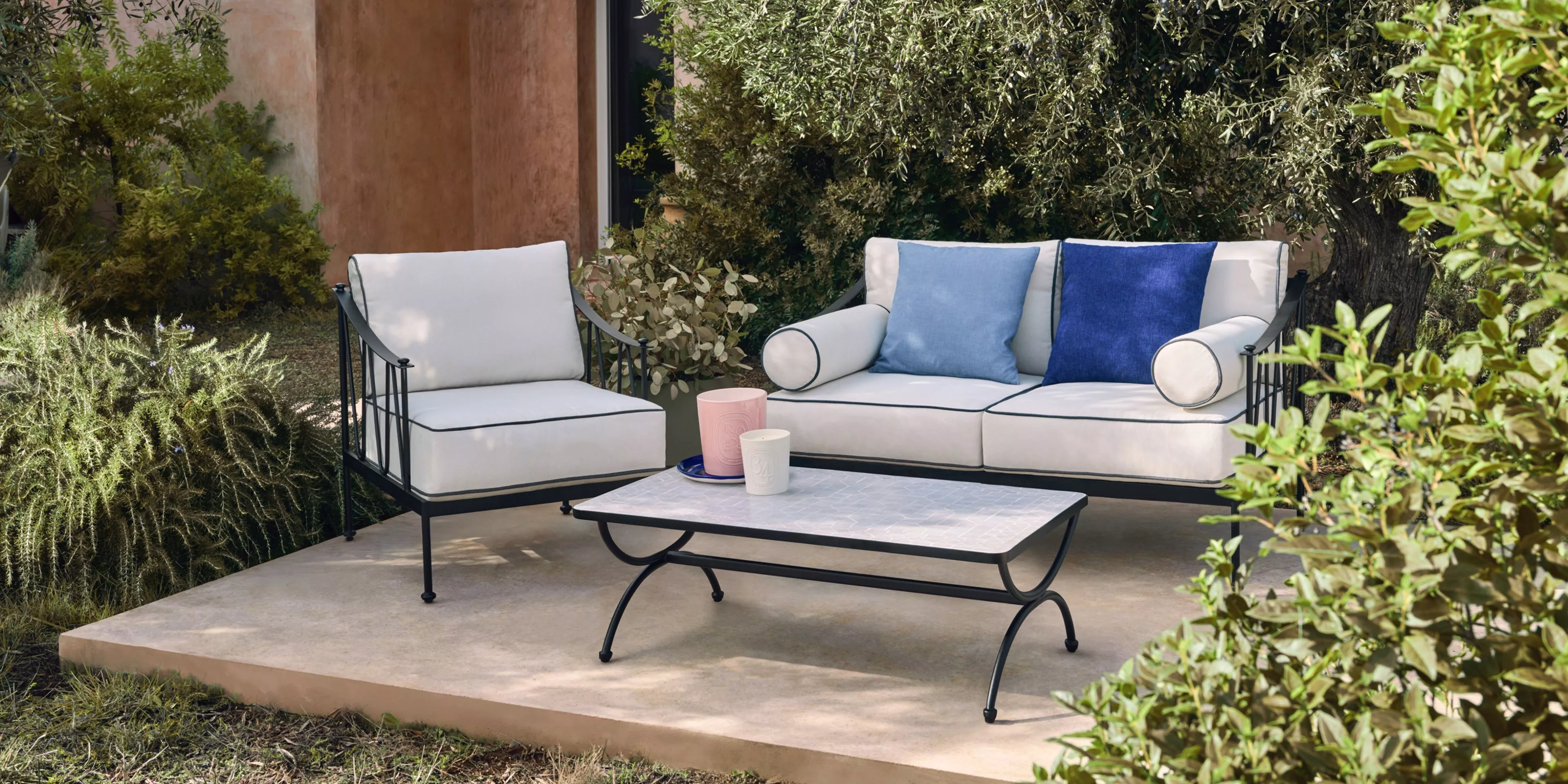 Outdoor garden lounge set with white sofa and armchair, blue cushions, and metal coffee table on patio