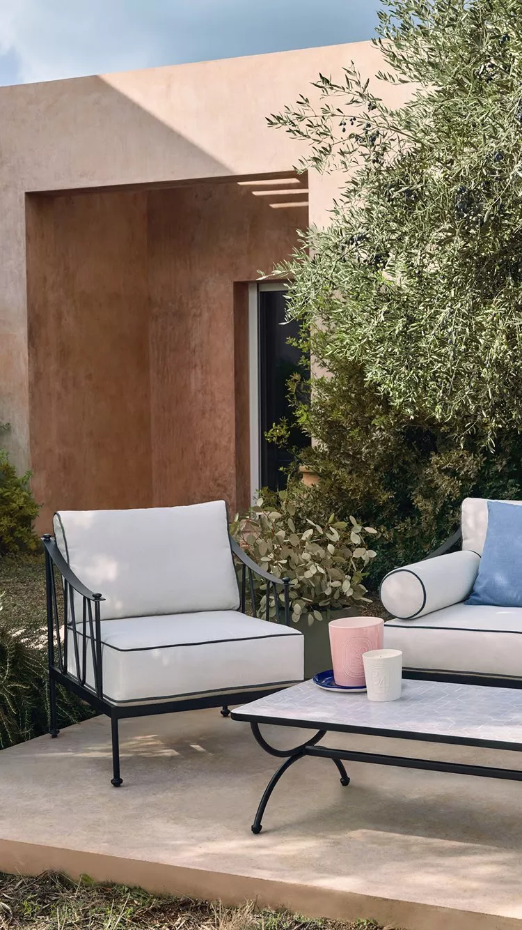 Outdoor patio lounge set with white cushions, blue pillows and coffee table in a leafy garden terrace.