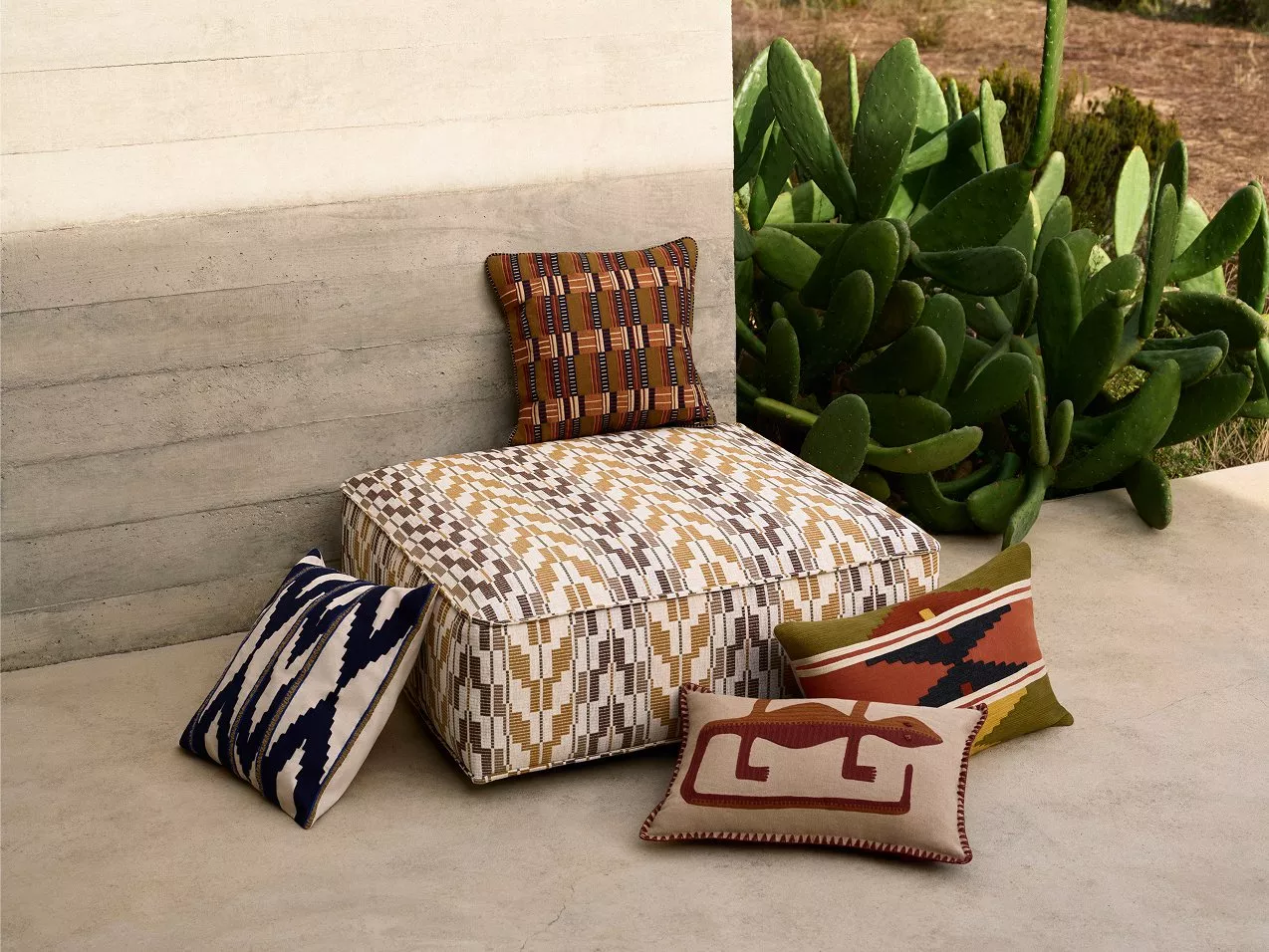 Sunlit modern patio lounge with cushioned armchair, sofa, round coffee table and colourful tea set indoors-outdoors